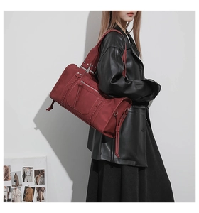 Detail of burgundy woven leather travel bag with long zipper pulls and slim strap