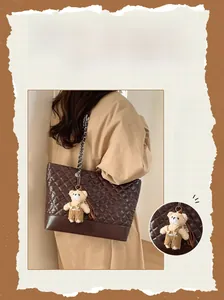 Detail of dark brown quilted tote bag with metal chain strap and teddy bear pendant