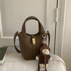 Close-up of a brown bucket bag with a plush bear charm on a soft fabric sofa