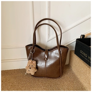 Detail of dark brown leather tote bag with plush bear charm and vintage texture