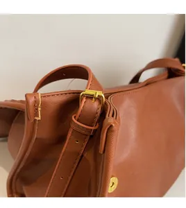 Detail of a brown leather bag showing the adjustable shoulder strap and gold metal buckle