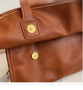 Detail of caramel lychee leather texture and circular gold magnetic buckle on a retro bag