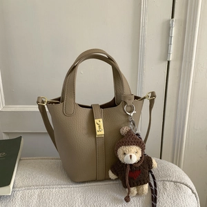 Detail of khaki leather bucket bag with gold lock and cute teddy bear plush charm