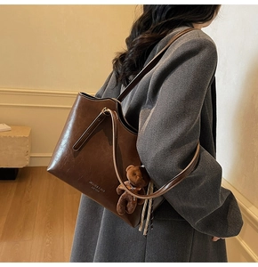 Detail of a large dark brown leather tote bag worn by a model in a gray suit jacket