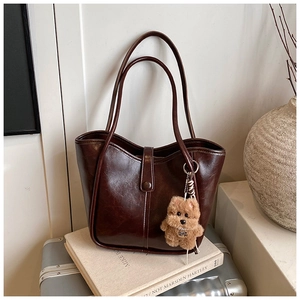 Detail of dark brown patent leather tote bag with fluffy puppy pendant on book