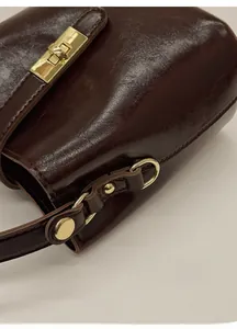 Detailed close-up of dark reddish-brown leather texture and polished gold hardware