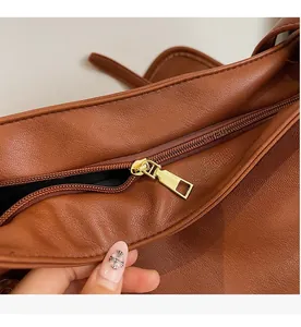 Close-up of smooth gold metal zipper and lychee textured leather on a brown messenger bag