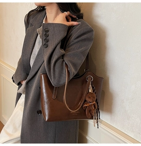 Detail of dark brown leather tote bag with plush bear charm and branding on coat