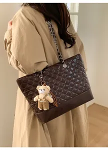 Detail of large brown quilted tote bag with chain strap and plush bear charm