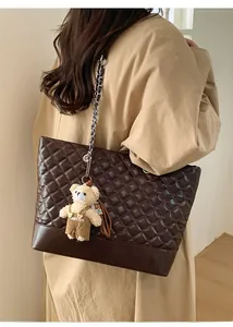 Detail of dark brown quilted tote bag with chain strap and teddy bear charm on model