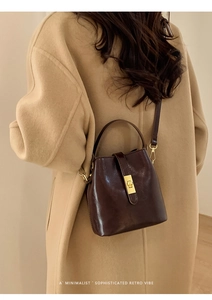 Détail d'un sac seau en cuir marron foncé avec boucle dorée sur manteau en laine