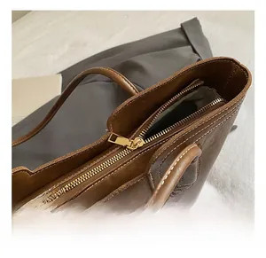 Detail der braunen Leder-Tote-Bag mit goldenem Reißverschluss und weißen Kontrastnähten