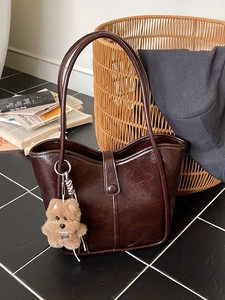Dark brown oil wax leather bucket bag with plush dog charm on a black tile surface