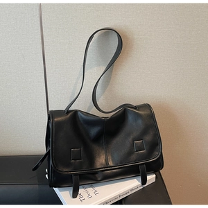 Detail of black leather messenger bag with pebble texture resting on art books
