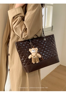 Detail of dark brown quilted tote bag with metal chain strap and bear charm accessory