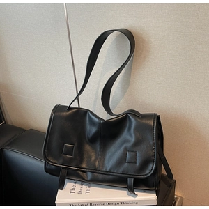 Detail view of smooth black faux leather messenger bag resting on design books