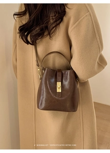 Brown retro bucket bag with gold square lock shown on a beige wool coat model