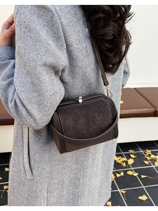 Detail view of a vintage dark brown suede shoulder bag with metallic buckle on a wool coat