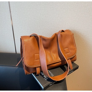 Close-up of brown soft leather messenger bag with flap closure on a black book prop