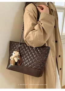 Detail of dark brown quilted tote bag with silver chain strap and teddy bear charm