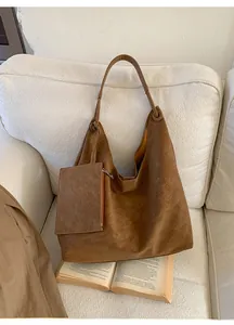 Close-up of brown leather tote bag with small pouch on a white sofa with vintage book
