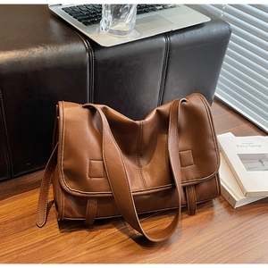 Brown vintage messenger bag placed on wooden floor with office laptop and books