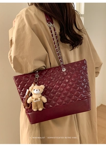 Detail of burgundy quilted tote bag with chain strap and teddy bear charm on model