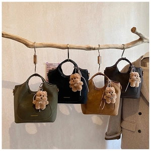 Detail view of four textured leather bucket bags hanging on a wooden branch with bear charms