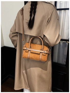 Sac bandoulière en daim marron porté avec un manteau kaki dans un décor intérieur épuré