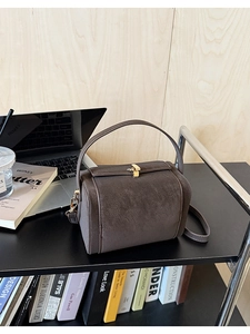 Close-up of vintage brown suede handbag with golden buckle on a wooden desk with office decor