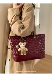 Detail of burgundy quilted tote bag with silver chain strap and cute teddy bear charm