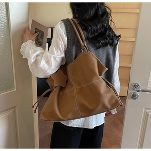 Detail of a large brown leather tote bag with white stitching and a star pendant