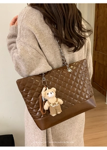 Detail of glossy quilted leather tote with silver chain strap and plush bear charm