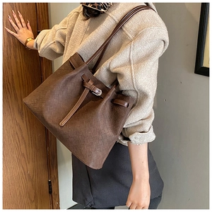 Detail of dark brown woven tote bag with adjustable strap shown on a shoulder