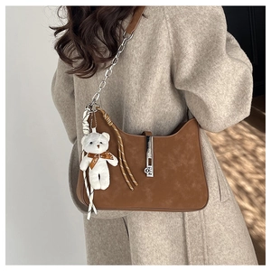Detail of a brown suede crescent bag with silver chain strap and a cute bear charm