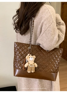 Detail view of brown quilted tote bag featuring a plush bear pendant and metal chain strap