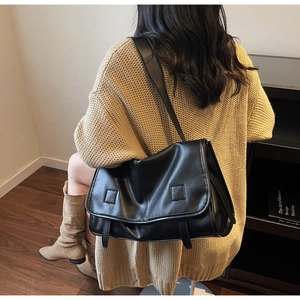 Detail of a large black matte leather messenger bag worn over the shoulder with a knit sweater