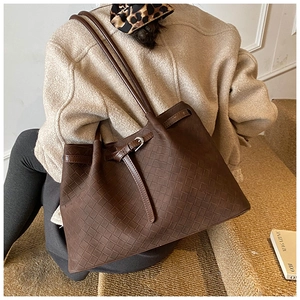 Detail of dark brown leather tote featuring woven texture and a metallic buckle closure