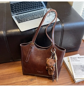 Close-up of vintage brown tote bag with gold logo, teddy charm, and tassel on leather sofa