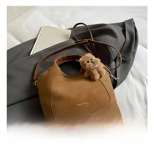 Detail of a brown leather bucket bag with gold lettering and a cute teddy bear charm