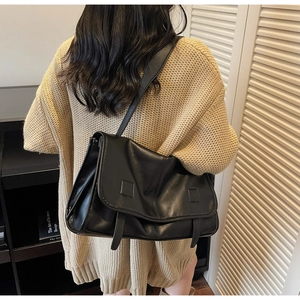 Detailed view of the large black vintage messenger bag worn with a beige sweater