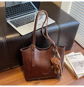 Close-up of brown vintage tote bag with bear charm and branding detail in cozy setting