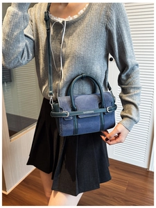 Détail du sac à bandoulière en daim bleu foncé avec poignées et finitions en cuir vert