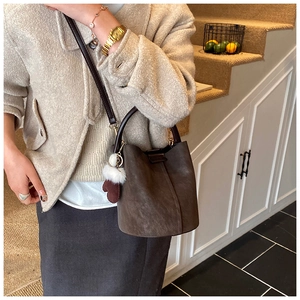 Detail view of a brown suede bucket bag with white pom-pom pendant on a model