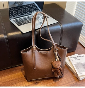 Close-up of dark brown PU leather tote bag featuring a cute plush bear charm and adjustable straps