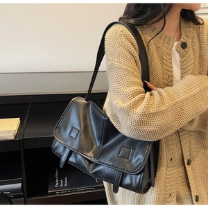 Side view of a vintage black PU leather messenger bag worn on shoulder by a model