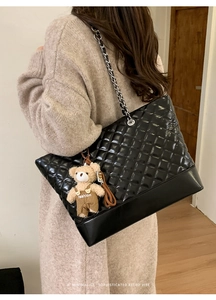 Detail of black quilted leather tote bag with silver chain strap and plush bear charm