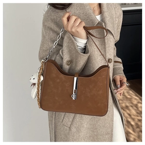 Detail of caramel brown suede shoulder bag with silver buckle and plush bear charm