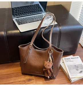 Detail of vintage brown tote bag with logo and cute plush bear charm on wooden floor