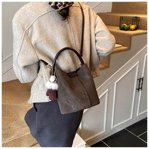 Detail of mocha brown faux suede bucket bag with decorative white fur ball and glove pendant